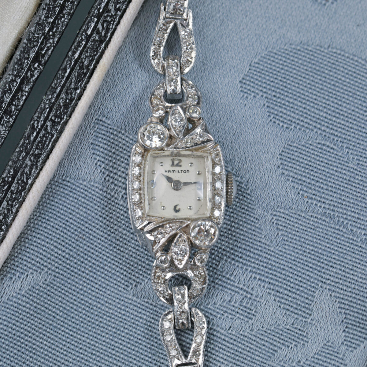 Zoomed in photo of a Vintage Hamilton platinum diamond watch displayed in a blue jewelry box featuring approximately 1.76 carats total weight of diamonds with a diamond band and pave diamond accents around the watch face