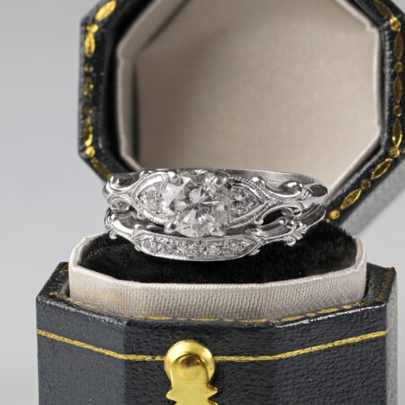 Platinum diamond wedding set displayed sitting on a ring box featuring a 0.62 carat round brilliant center diamond with sparkling accent diamonds along the engagement ring and matching band.