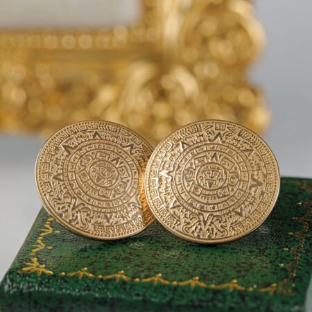 Pair of retro 18K yellow gold Aztec disc earrings sitting on a green box featuring bold geometric circular designs inspired by ancient motifs and sculptural styling.