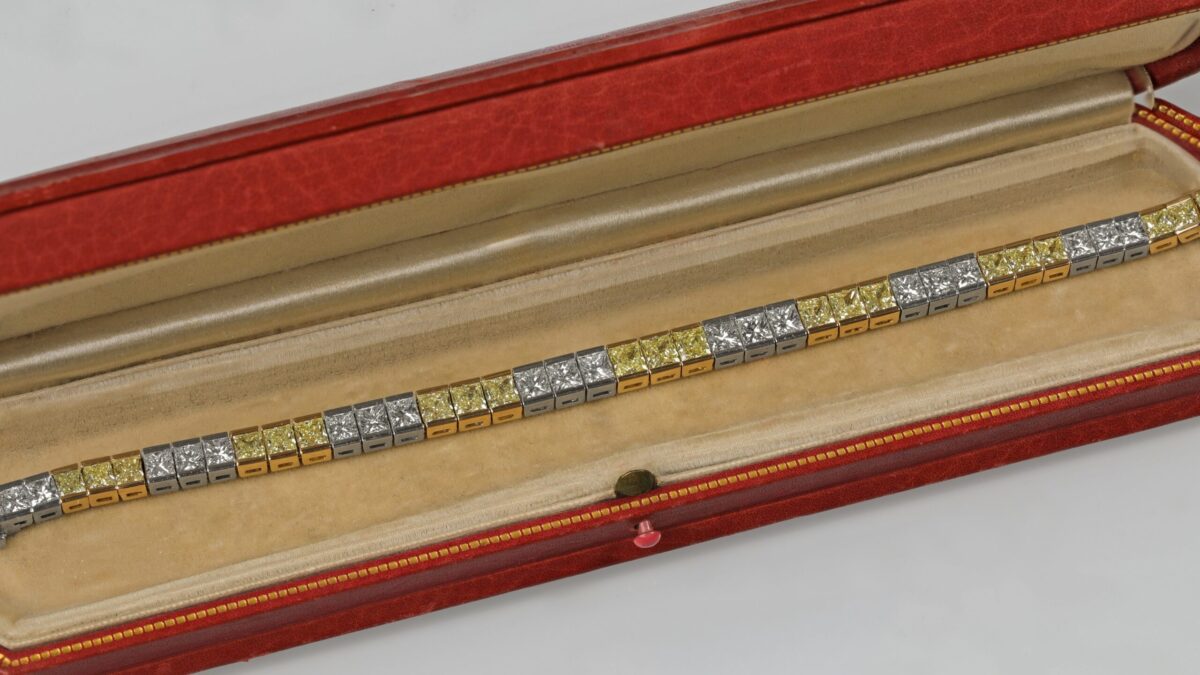 Yellow and white diamond tennis bracelet displayed in a red jewelry box featuring alternating fancy yellow and white diamonds in an elegant tapered design crafted in 18K yellow gold and platinum.