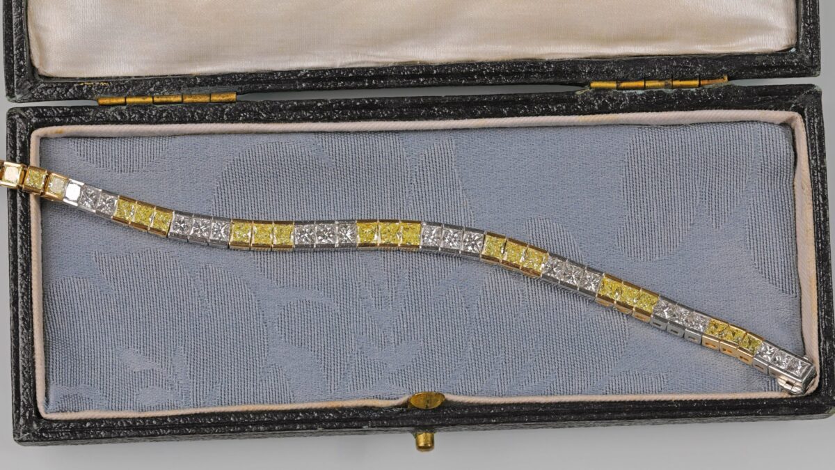 Yellow and white diamond tennis bracelet displayed in a blue jewelry box featuring alternating fancy yellow and white diamonds in an elegant tapered design crafted in 18K yellow gold and platinum.