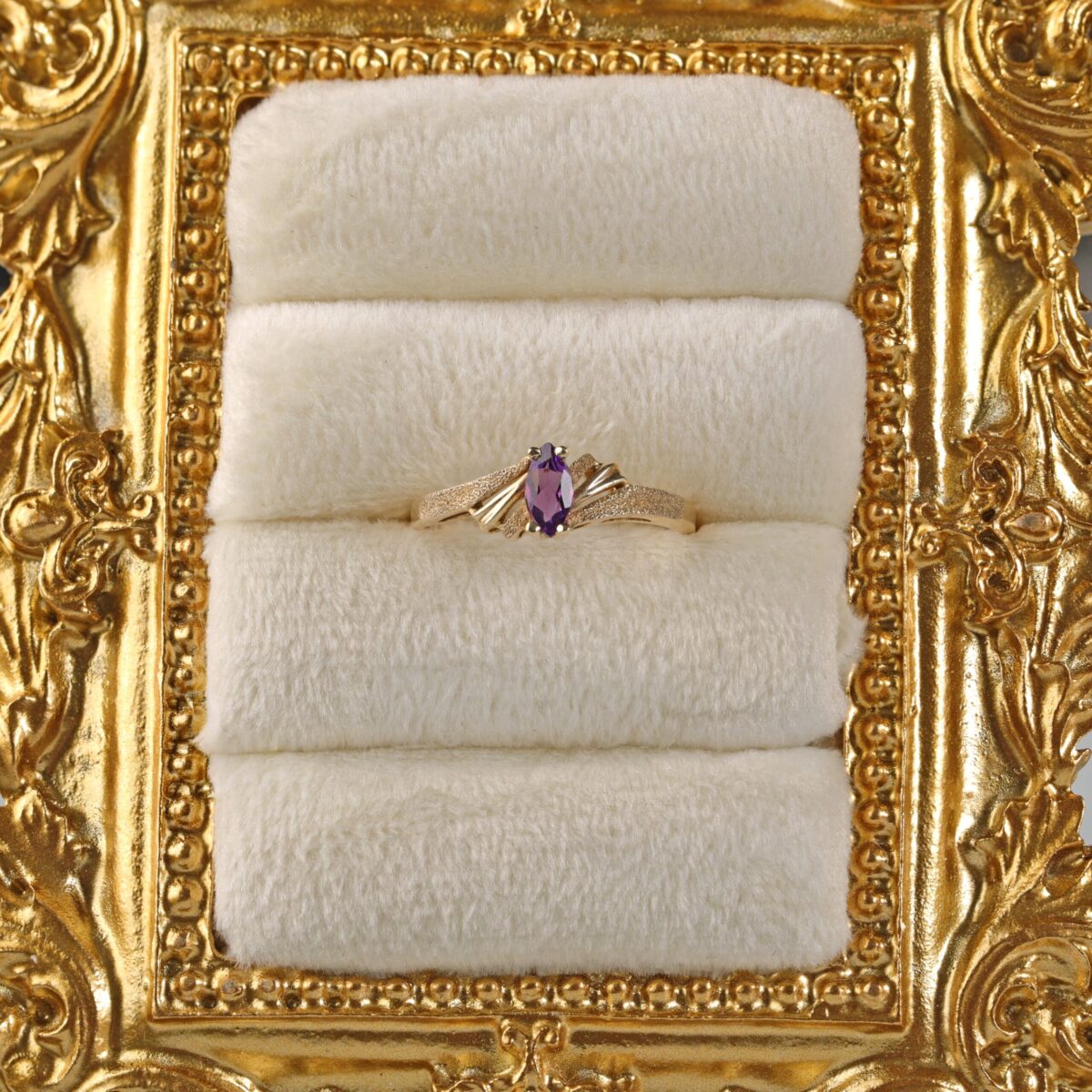 14K yellow gold amethyst ring displayed in a jewelry frame featuring a marquise cut amethyst with rich purple color in a delicate solitaire setting.