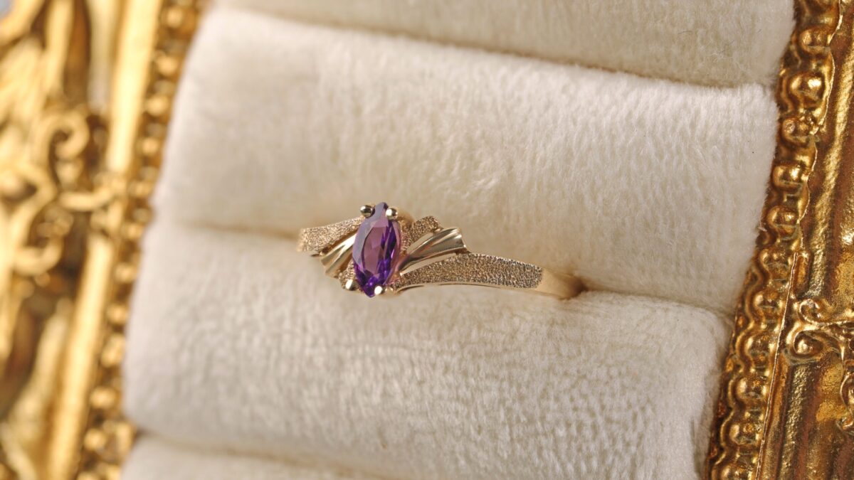 14K yellow gold amethyst ring displayed in a jewelry frame featuring a marquise cut amethyst with rich purple color in a delicate solitaire setting.
