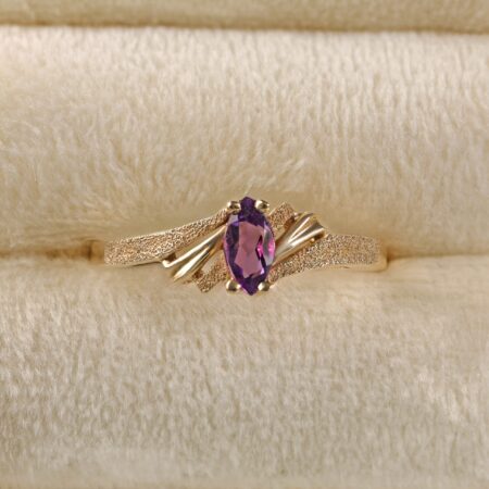 14K yellow gold amethyst ring displayed in a jewelry frame featuring a marquise cut amethyst with rich purple color in a delicate solitaire setting.