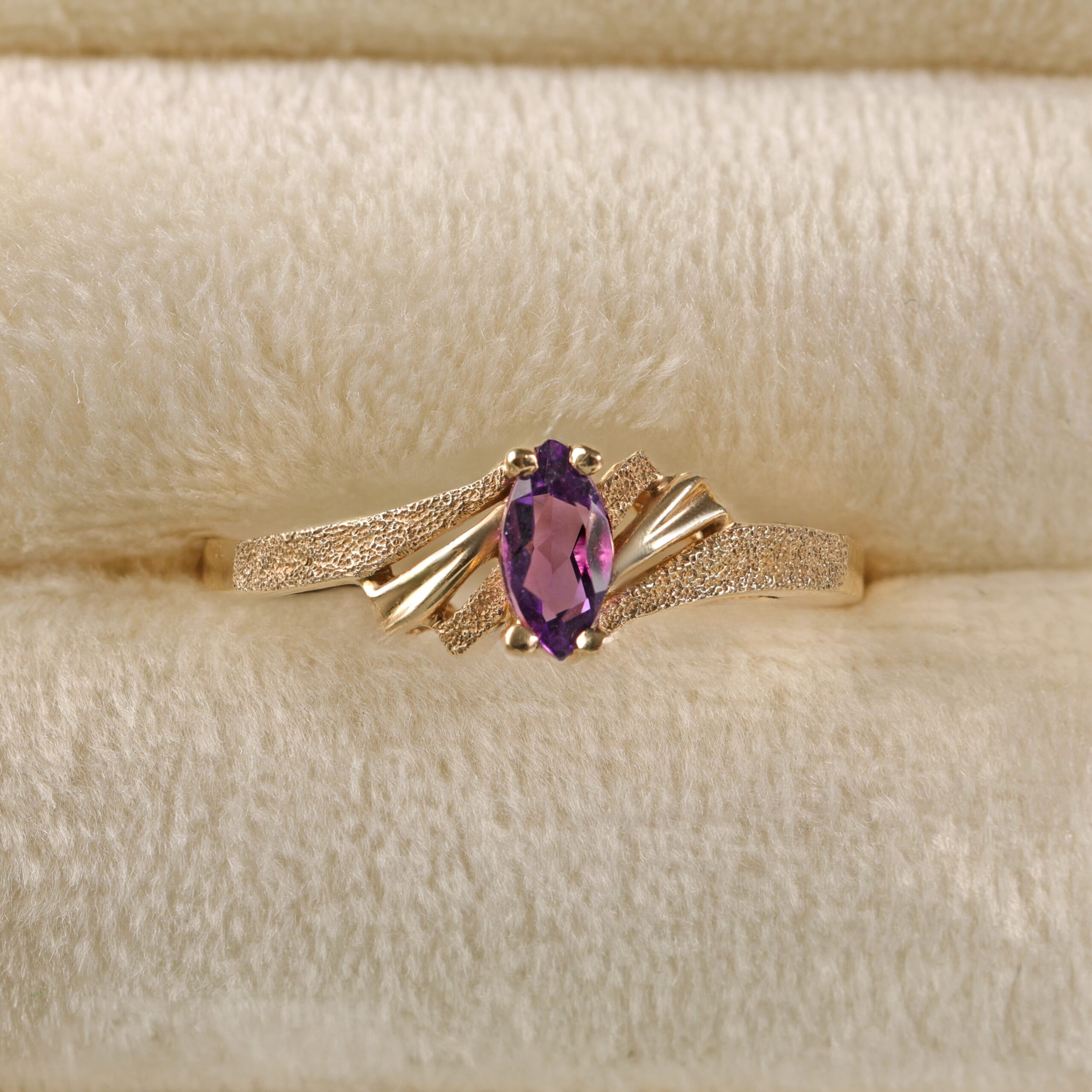 14K yellow gold amethyst ring displayed in a jewelry frame featuring a marquise cut amethyst with rich purple color in a delicate solitaire setting.